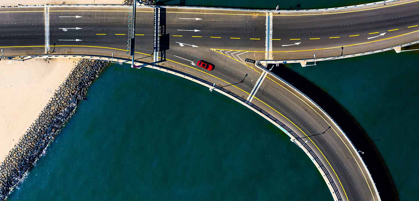 Highway section above water with red car traversing Highway section above water with red car traversing